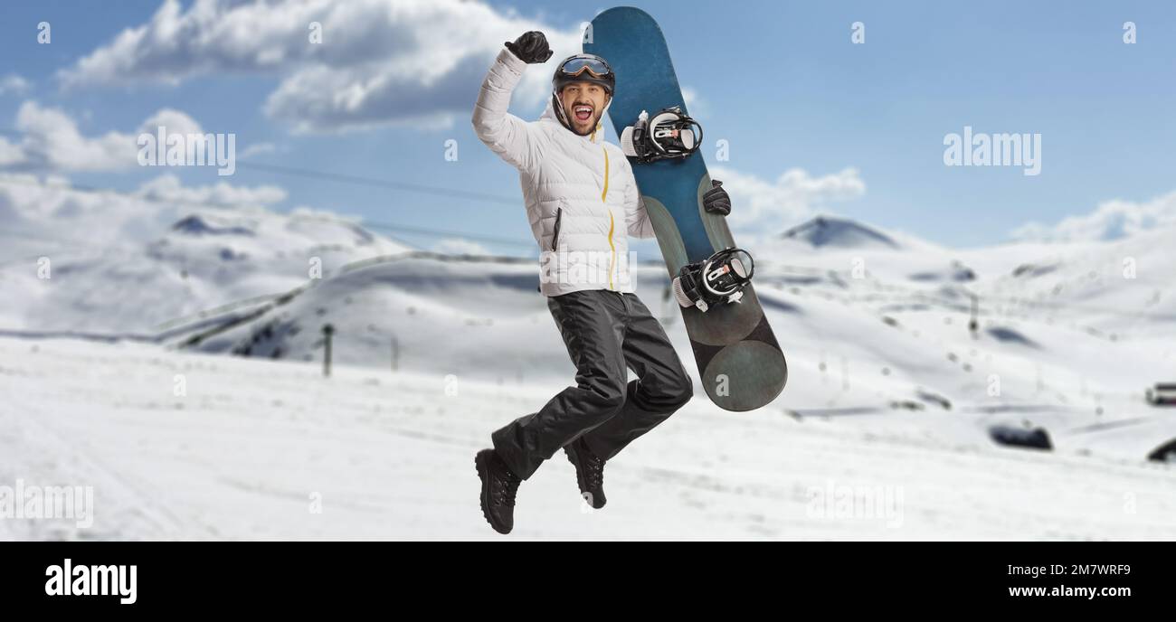 Happy man with a snowboard jumping and gesturing happiness on a snowy mountain Stock Photo