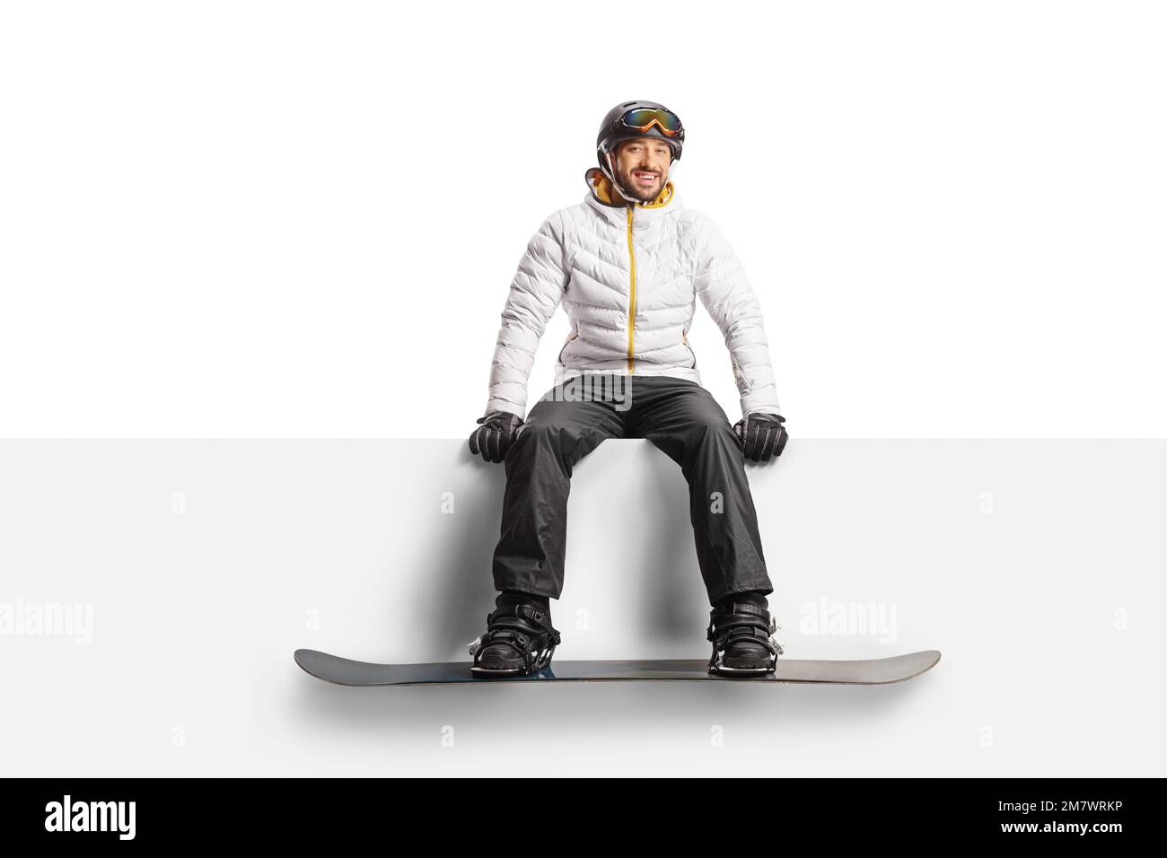 Man wearing a snowboard and sitting on a blank panel isolated on white background Stock Photo