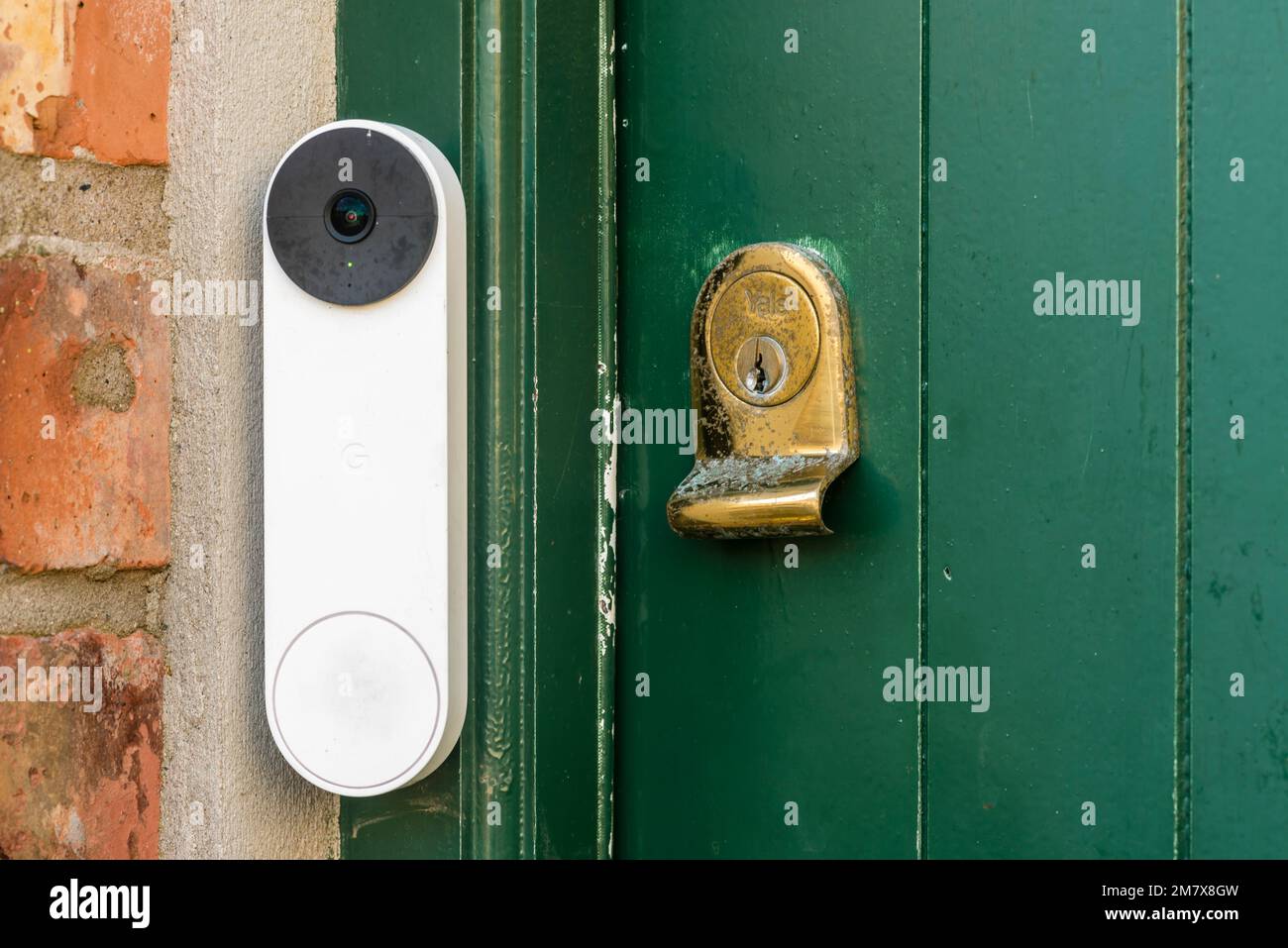 A Google Nest video doorbell on a green door with a brass Yale lock, United Kingdom, UK Stock Photo