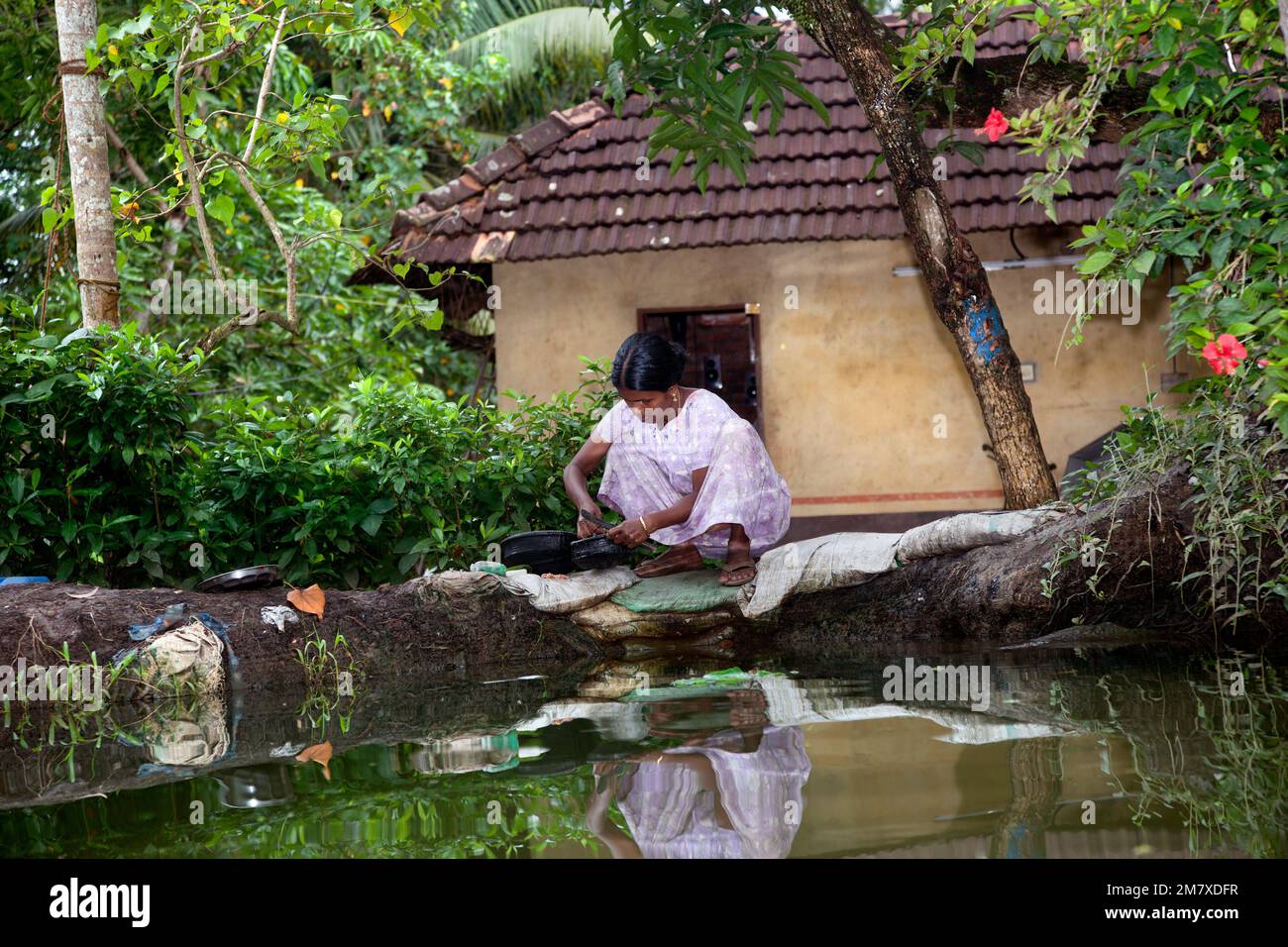 Allepy, India-September 7, 2012. Indian woman washes dishes and cutlery on the edge of one of the canals of Alappuzha Stock Photo