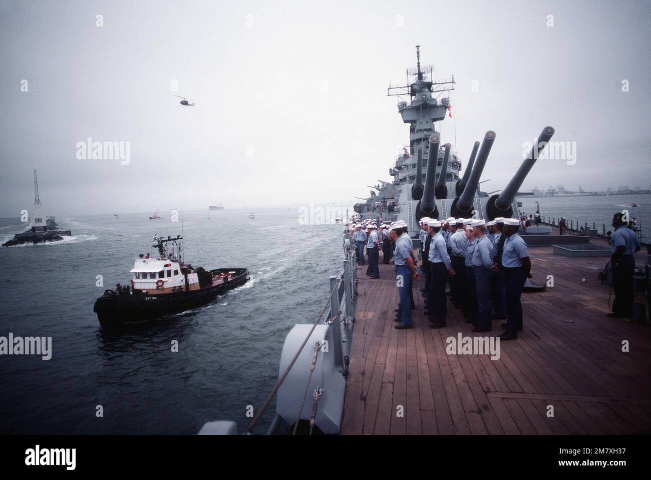 The crew stands in formation on the deck of the battleship USS NEW