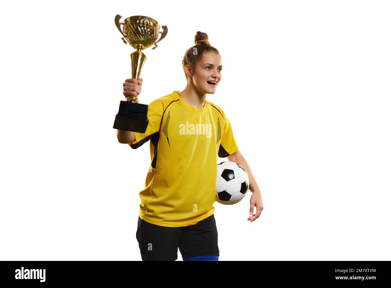 Young woman, professional female football, soccer player in yellow uniform posing with trophy and ball isolated over white studio background Stock Photo