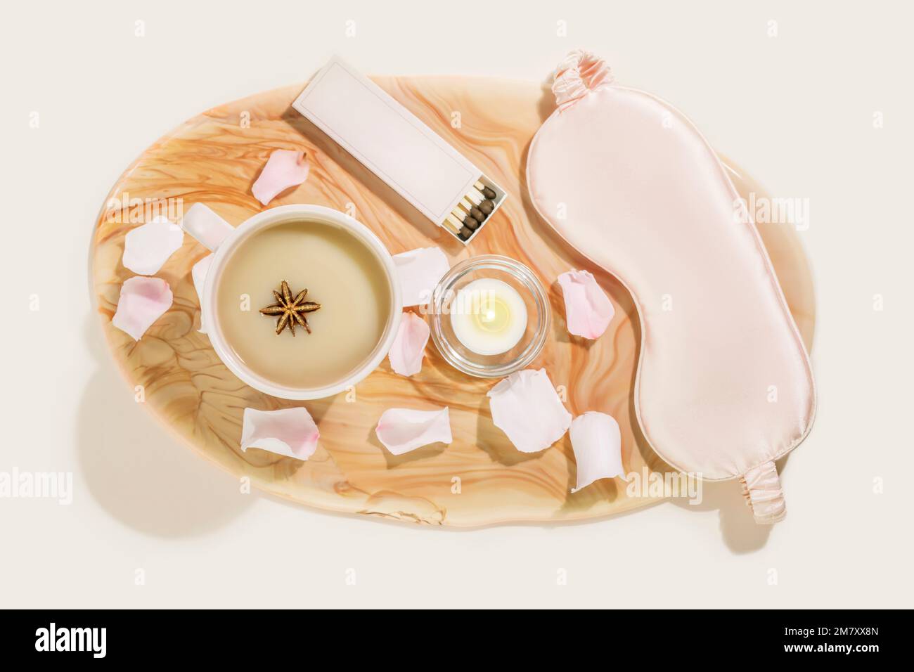 Sleep care flat lay with mask for sleep, cup of tea with milk, candle and rose petals on pink marble tray. Concept of relaxing at home, self care, slo Stock Photo