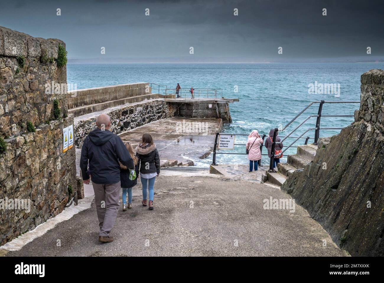 UK weather. Visitors walking down a slipway to The Wharf on a rainy chilly miserable day in the historic seaside town of St Ives in Cornwall in the UK Stock Photo