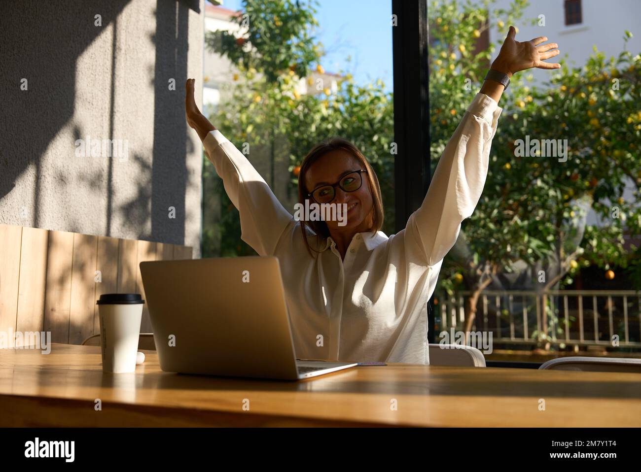 Exhausted businesswoman stretching with arms raised while working in coworking office. Stock Photo