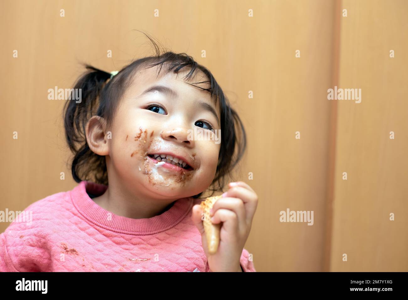 A happy toddler child eating chocolate ice cream in a cone with messy