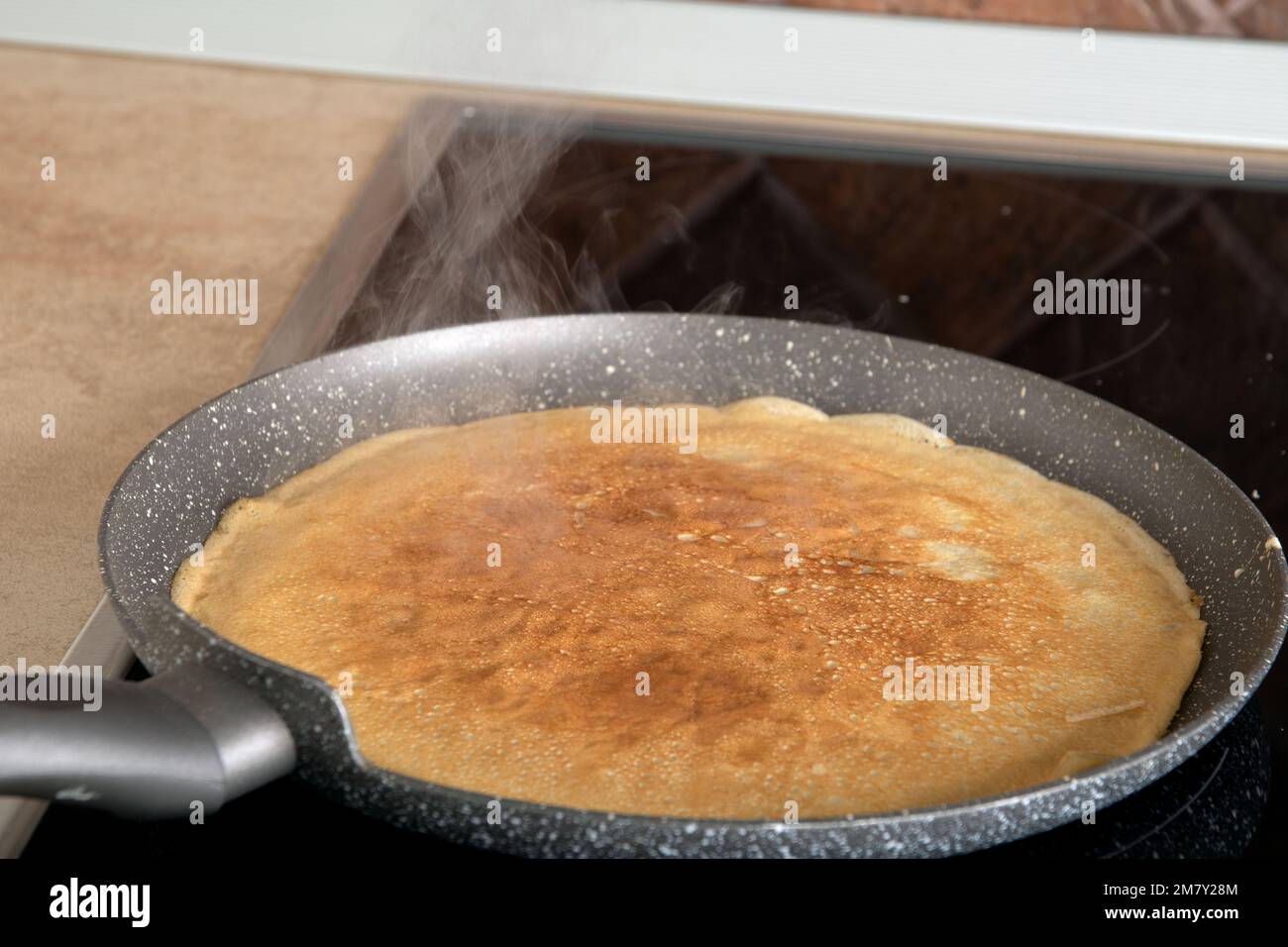 photo of a thin pancake frying on a pancake pan in the kitchen Stock
