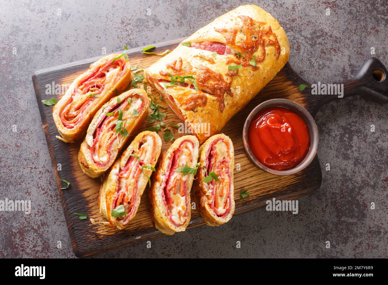Delicious pizza stromboli roll stuffed with salami sausage and mozzarella cheese close-up on a wooden board on the table. horizontal top view from abo Stock Photo