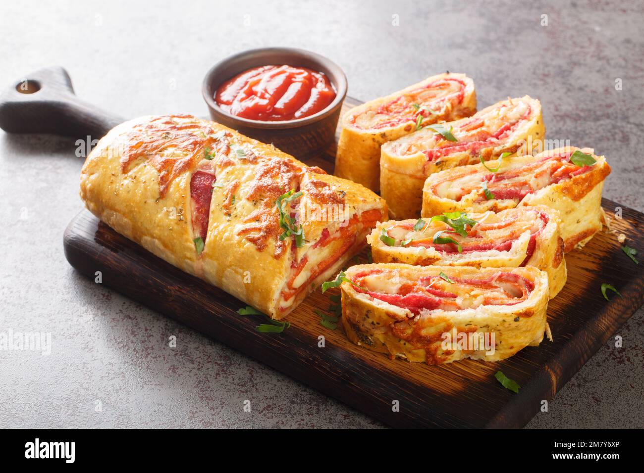 Italian stromboli, delicious pizza roll filled with sausage and ham closeup on the wooden board on the table. Horizontal Stock Photo