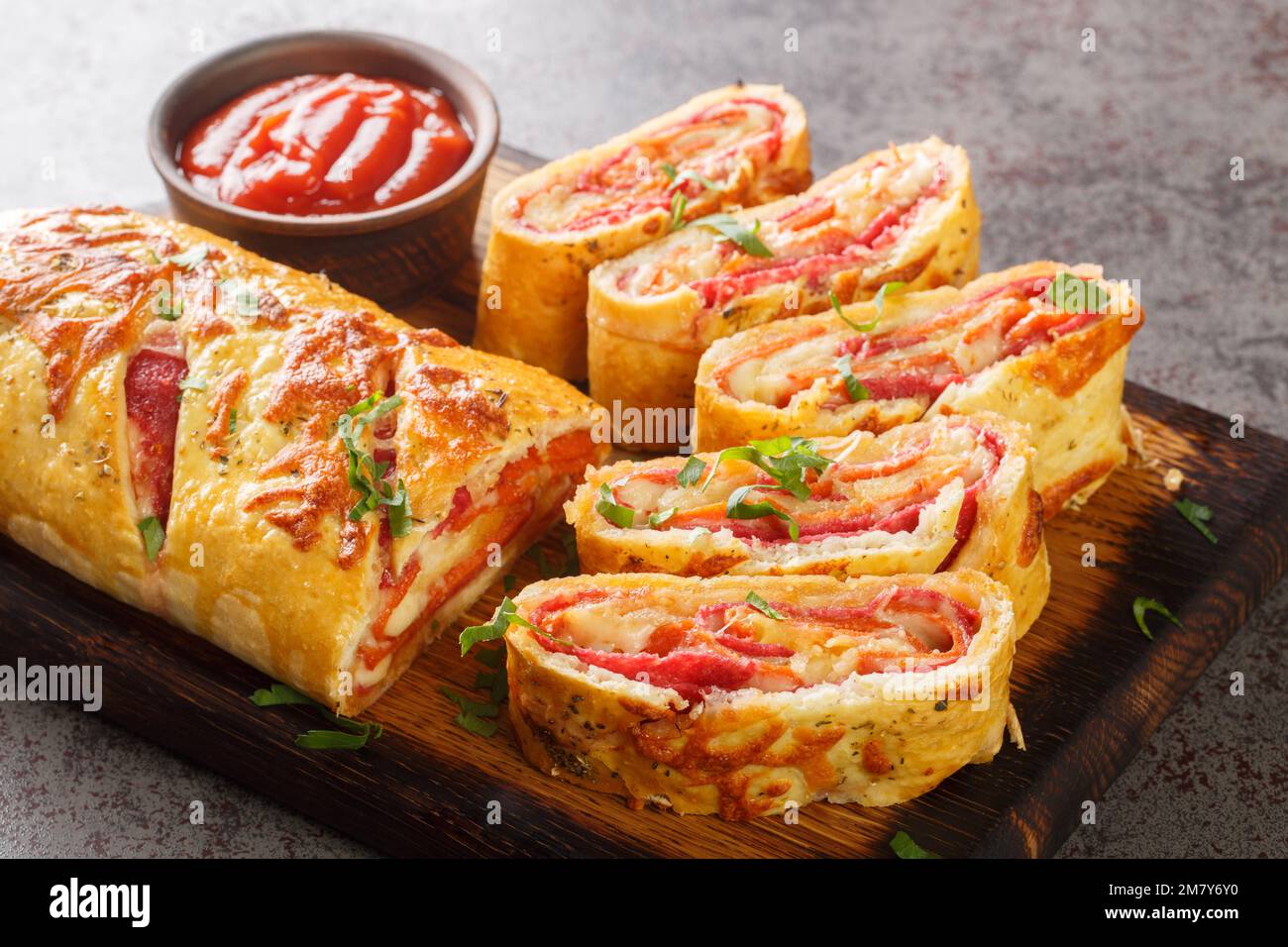 Delicious pizza stromboli roll stuffed with salami sausage and mozzarella cheese close-up on a wooden board on the table. horizontal Stock Photo