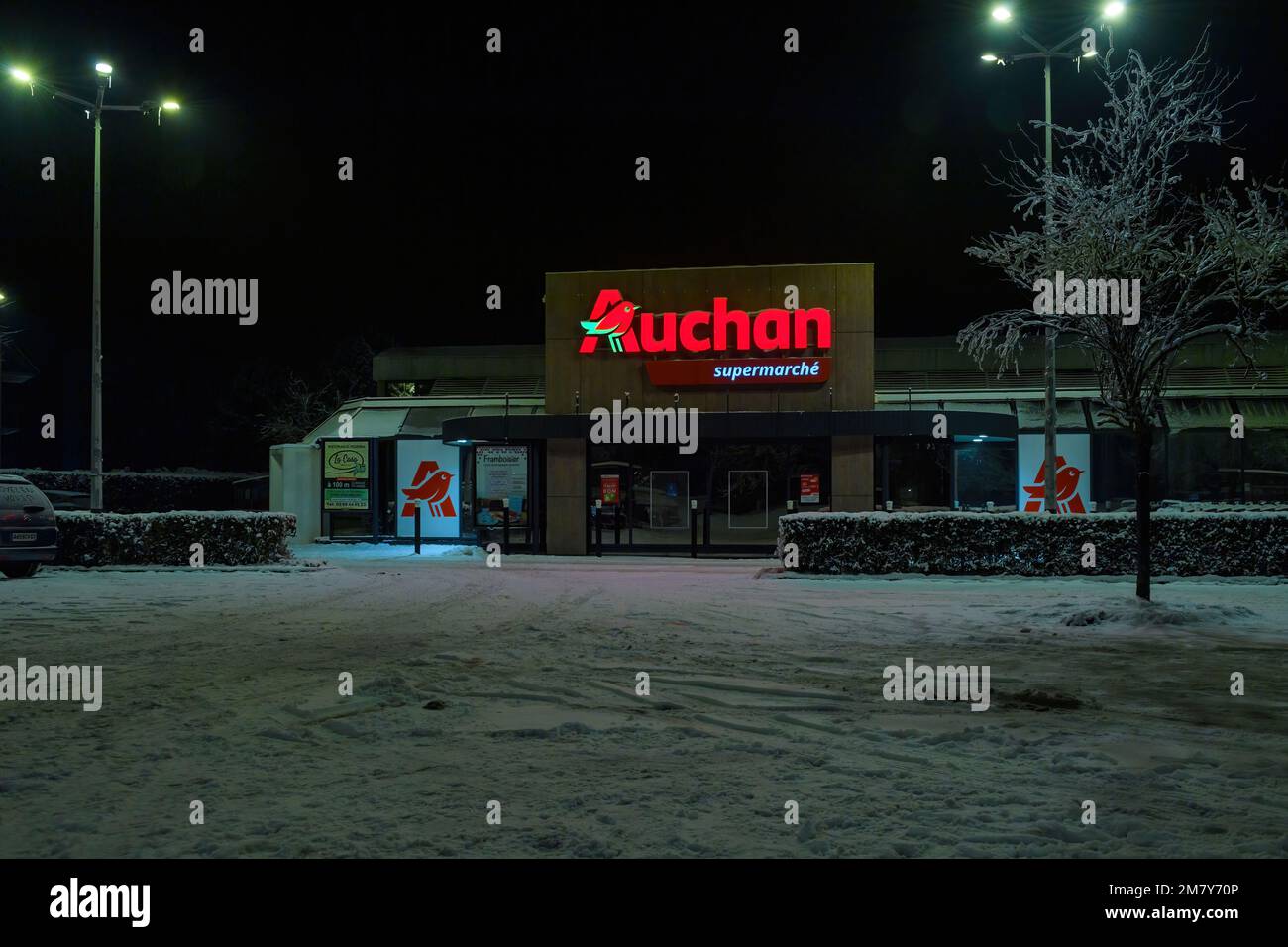 Strasbourg, France - Dec 19, 2022: Closed Auchan supermarket late at night - covered with snow asphalt parking Stock Photo
