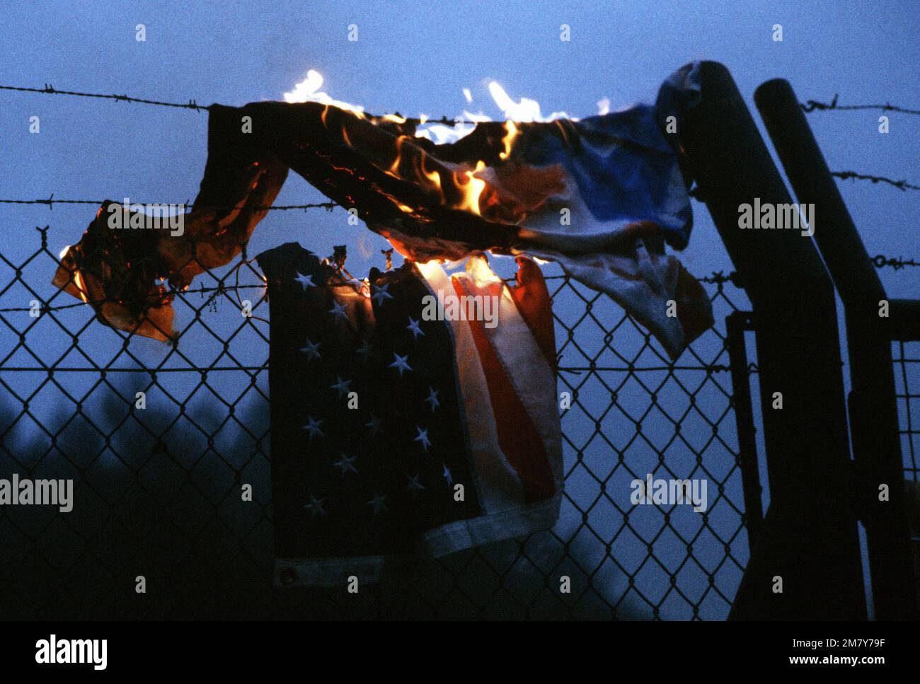 An American flag is burned on the perimeter fence by protesters demonstrating against NATO's decision to deploy Pershing II and cruise missiles in Western Europe. Base: Rhein-Main Air Base Country: Deutschland / Germany (DEU) Stock Photo