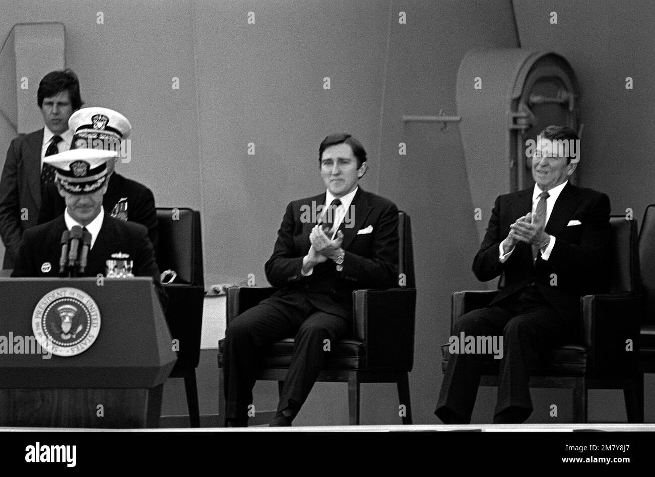 President Ronald Reagan, right, and Secretary of the Navy John Lehman Jr. applaud as CAPT William M. Fogarty, commanding officer, speaks during the recommissioning ceremony for the battleship USS NEW JERSEY (BB-62). Base: Long Beach Naval Shipyard State: California (CA) Country: United States Of America (USA) Stock Photo