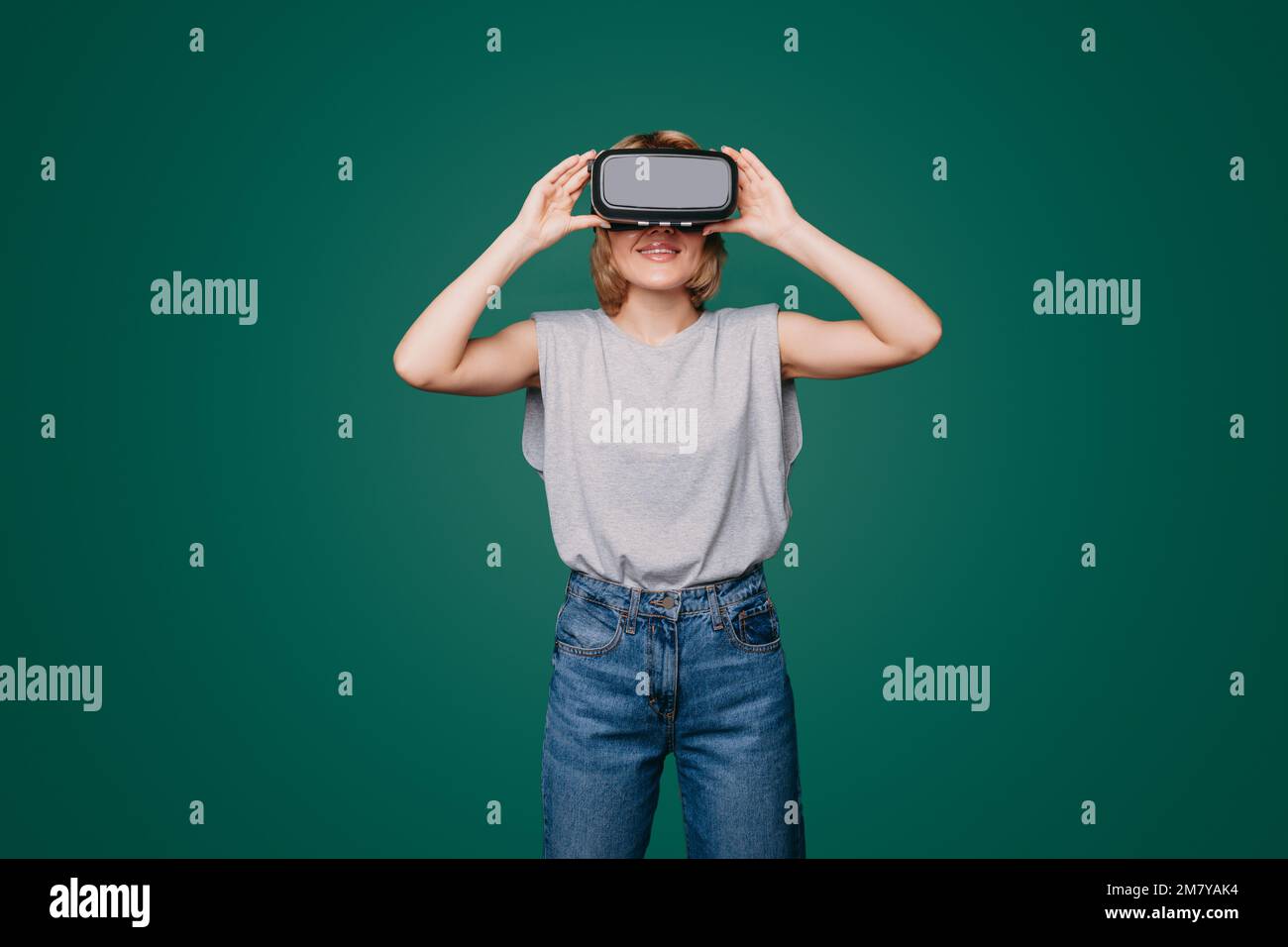 Beautiful young woman using technologic goggles posing on green background. Metaverse digital world technology. Modern technology. Future digital Stock Photo