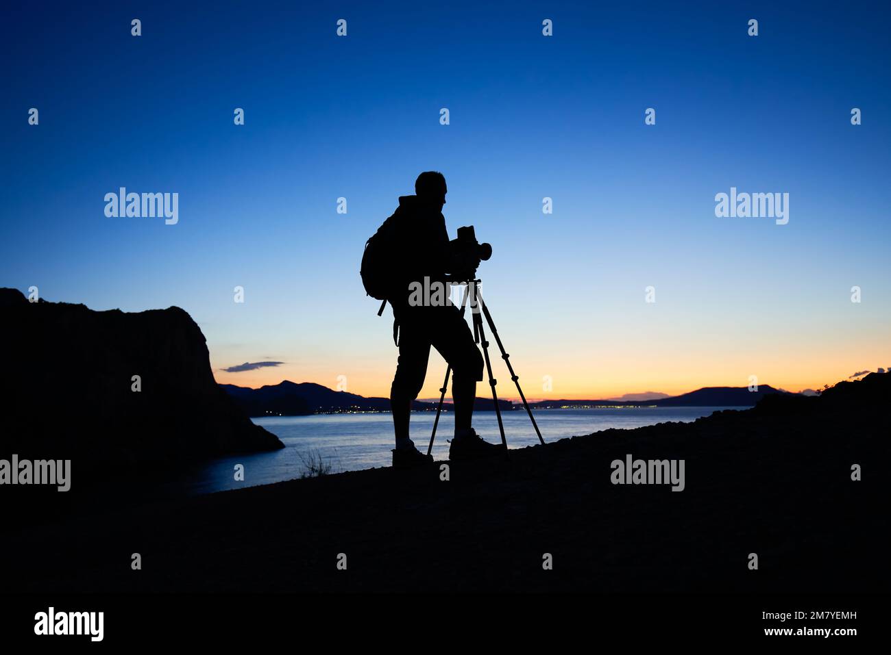 Silhouette of photographer on top of mountain at sunset background. Nature photographer in the action. Film analog photography Stock Photo