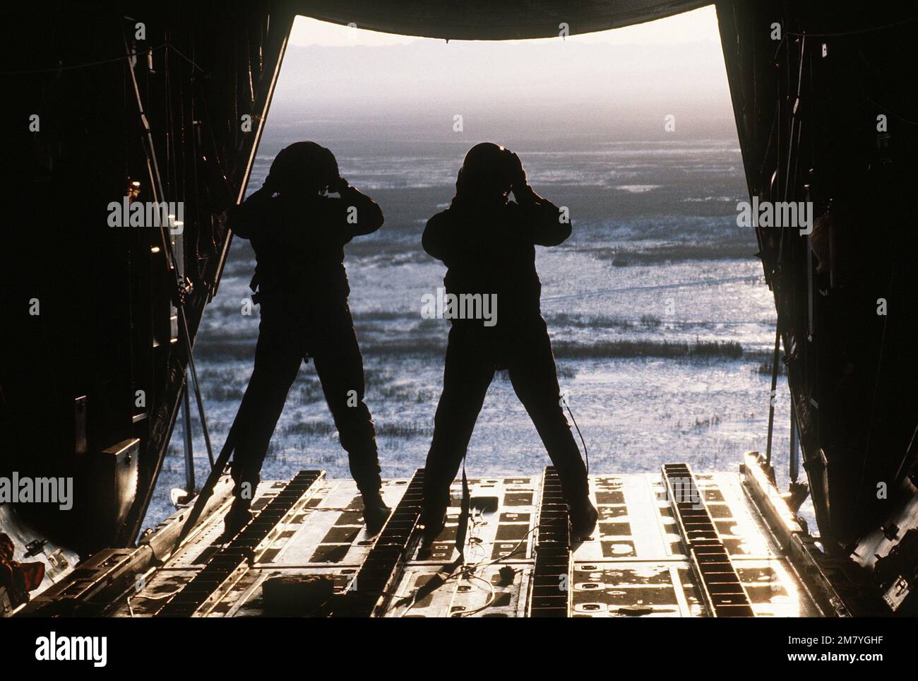 Crewmen watch from the cargo opening of a C130 Hercules aircraft as a