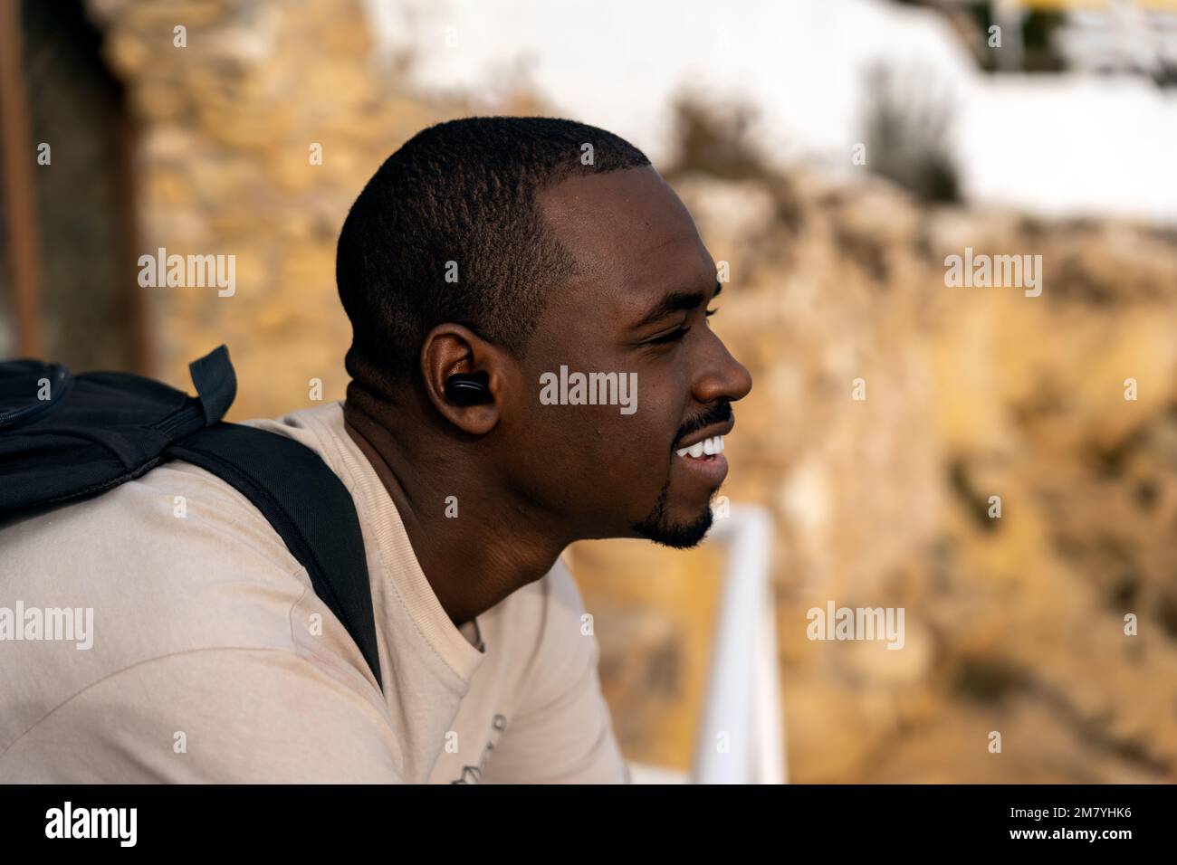 Positive black male traveler in casual clothes with backpack leaning on railing and looking away while spending time on viewpoint on beach Stock Photo