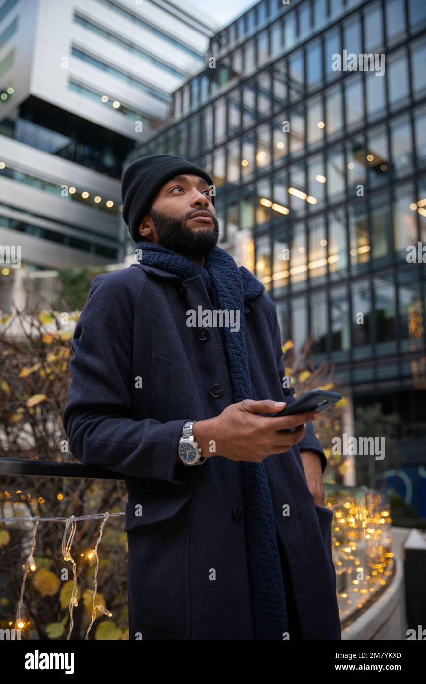 African businessman looks up with a thoughtful expression and holds his phone Stock Photo