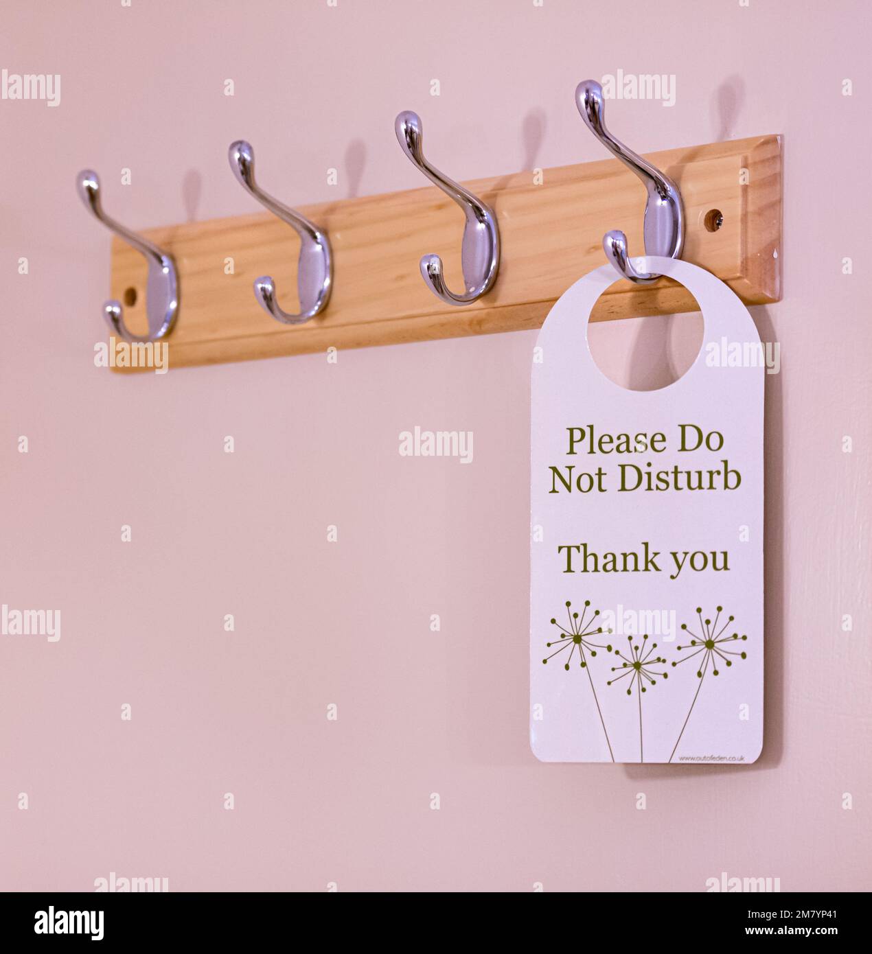 A 'Please Do Not Disturb' tag hanging on one of four clothes hooks. Stock Photo