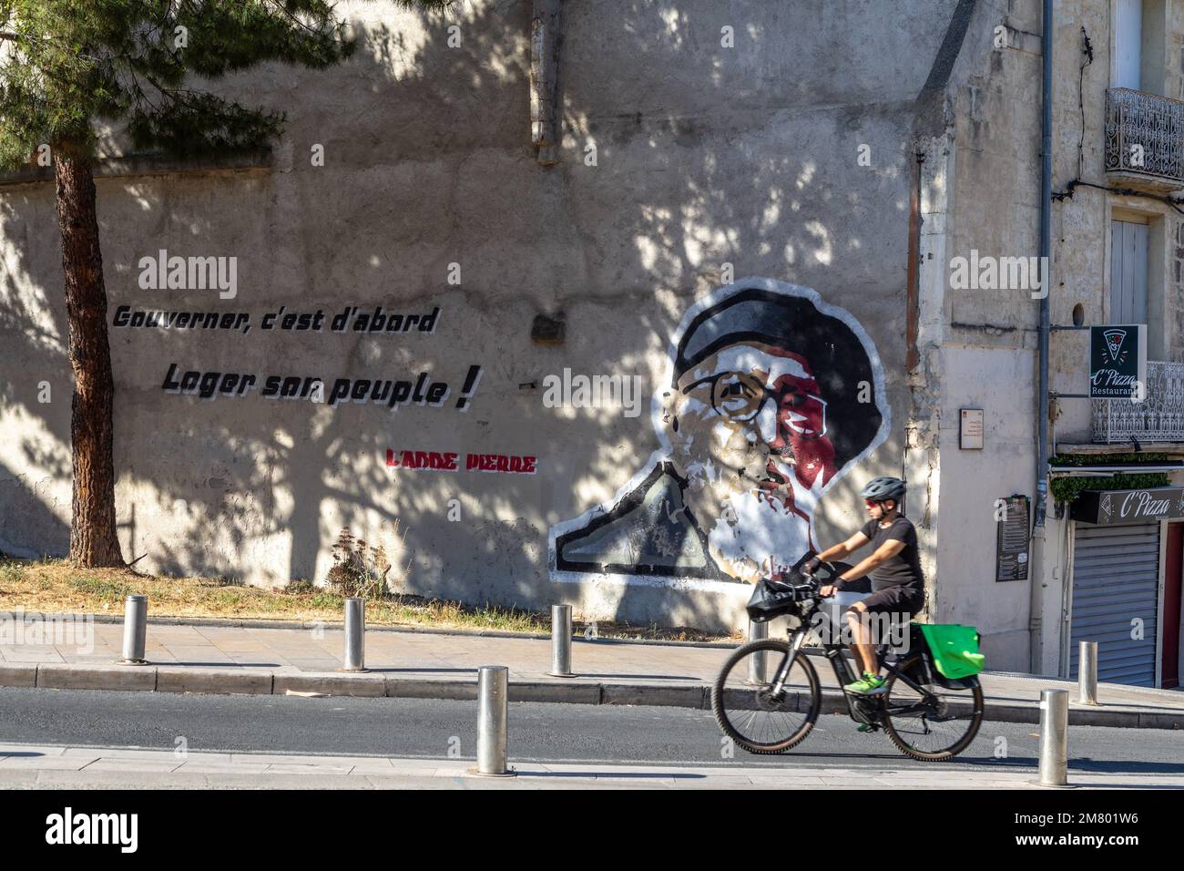 BICYCLE IN FRONT OF THE MURAL OF MURALE DE ABBE PIERRE, GOUVERNER, C'EST D'ABORD LOGER SON PEUPLE (TO GOVERN MEANS FIRST HOUSING ITS PEOPLE), RUE DU FAUBOURG DE NIMES, MONTPELLIER, HERAULT, OCCITANIE, FRANCE Stock Photo