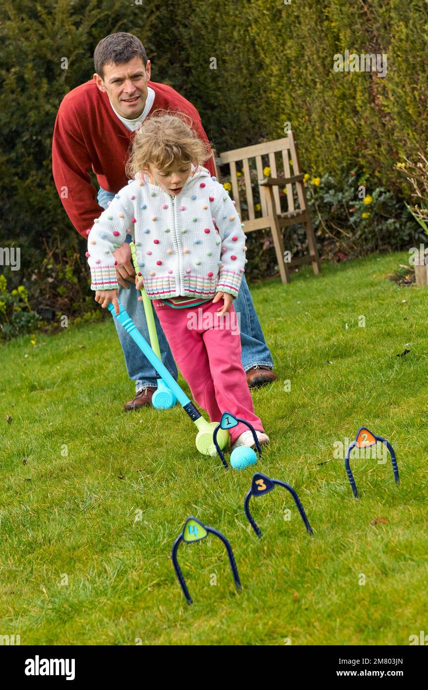 Adult male teaching a young girl how to play croquet in an English