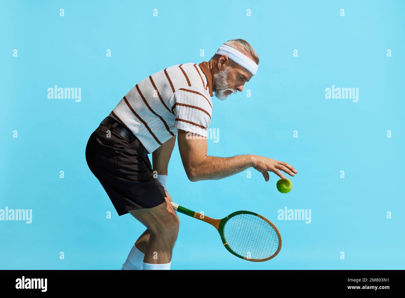 Portrait of handsome senior man in special uniformt playing tennis over blue background. Game preparation. Concept of leisure activity, hobby Stock Photo