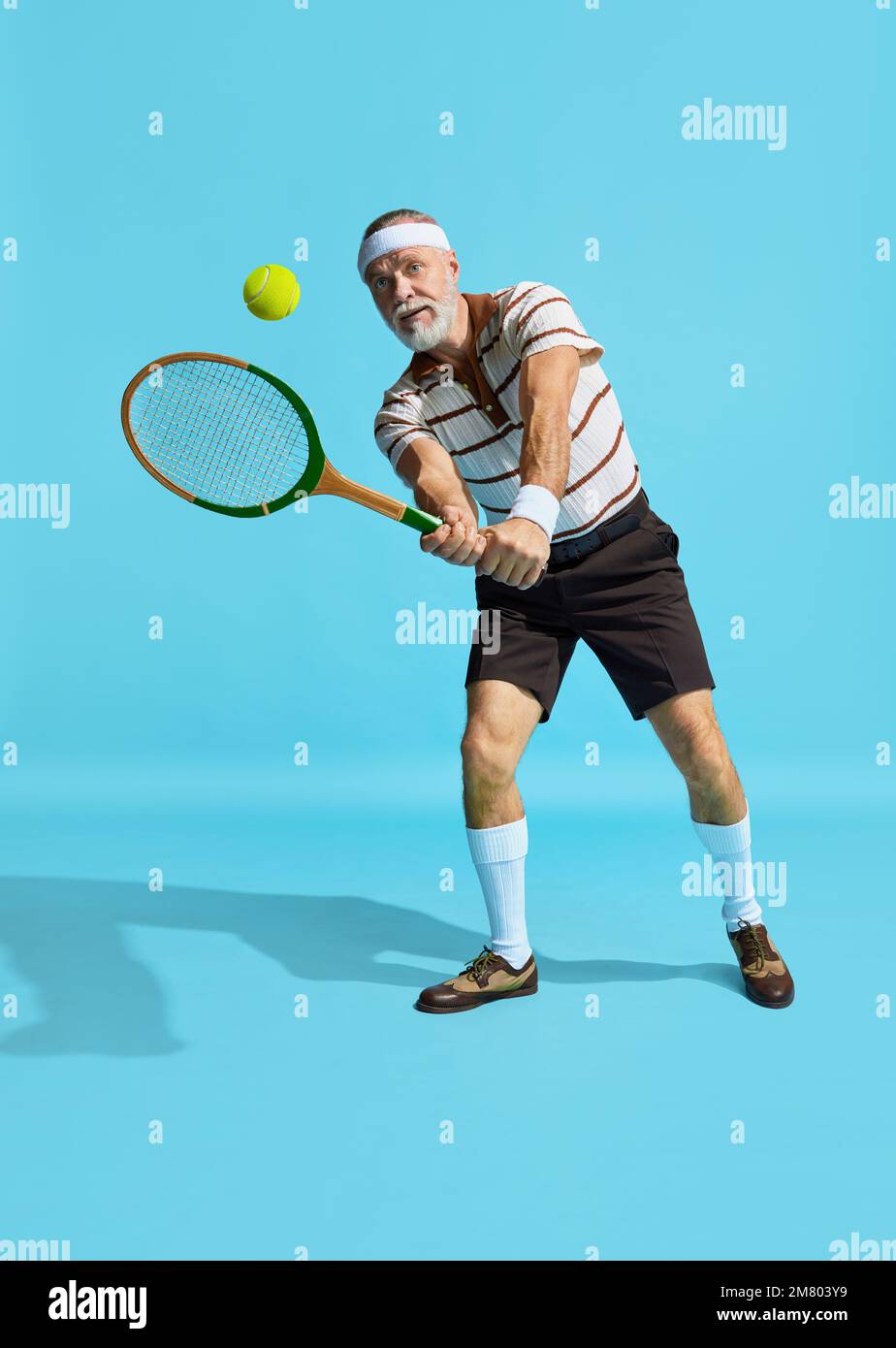 Active game. Portrait of handsome senior man in special uniformt playing tennis over blue background. Concept of leisure activity, hobby, lifestyle Stock Photo