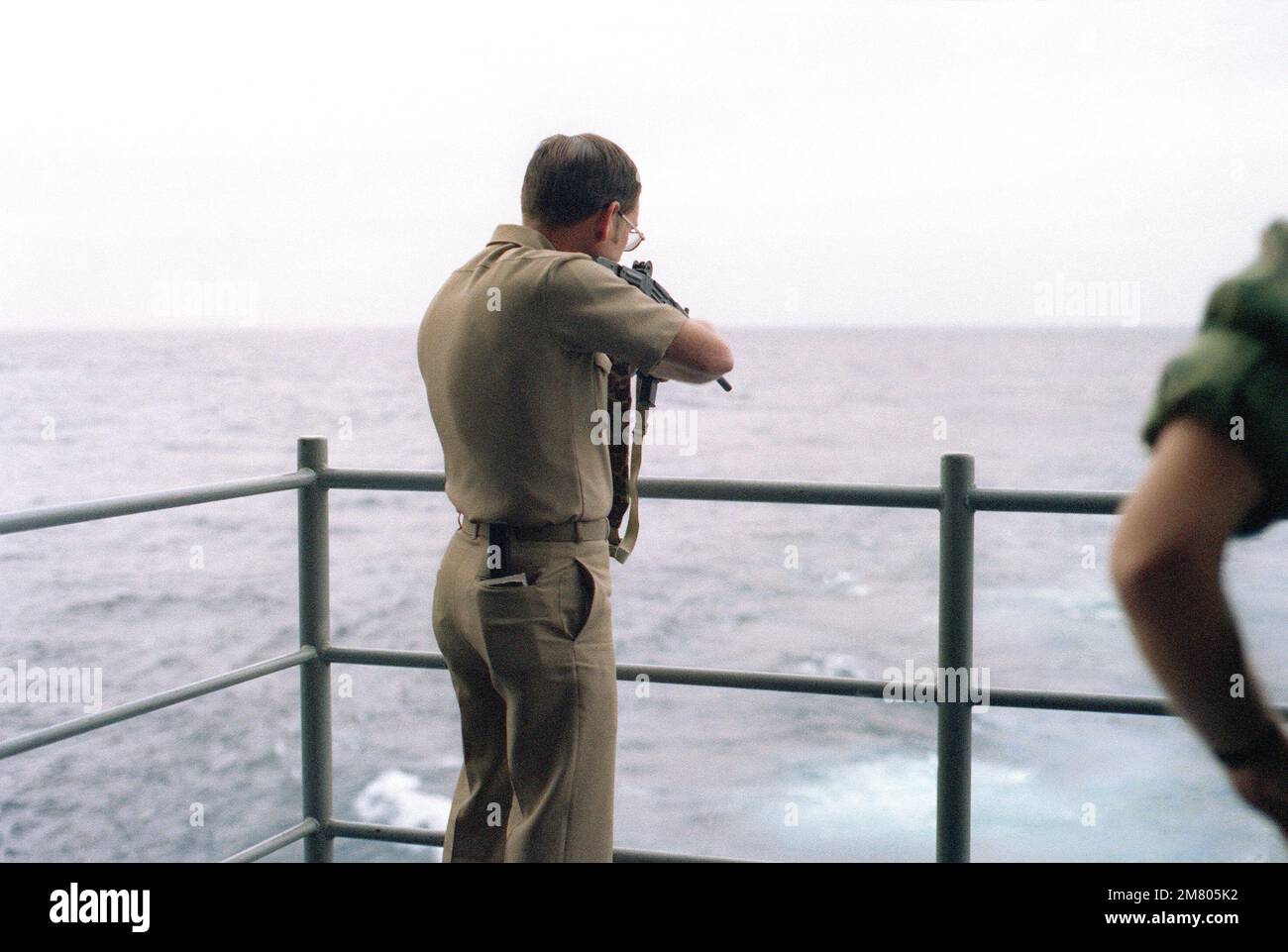 A Navy officer fires an Uzi 9 mm submarine gun off the fantail of the aircraft carrier USS KITTY HAWK (CV 63) during a familiarization weapons firing exercise. Base: USS Kitty Hawk (CV 63) Stock Photo