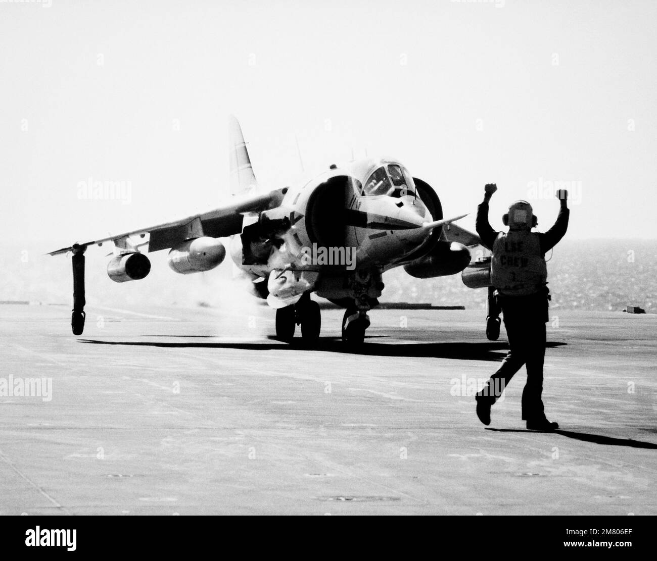 A flight deck crewman signals to the pilot of a AV-8C Harrier 