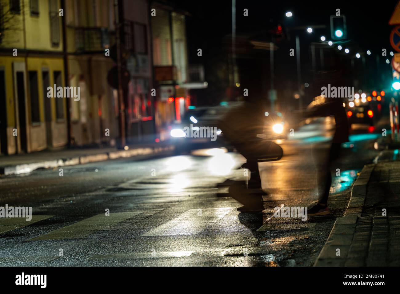 City street night blurred background. Dark dressed pedestrians crossing the street at night.. Bokeh night city life. The city of Ustrzyki Dolne, Polan Stock Photo