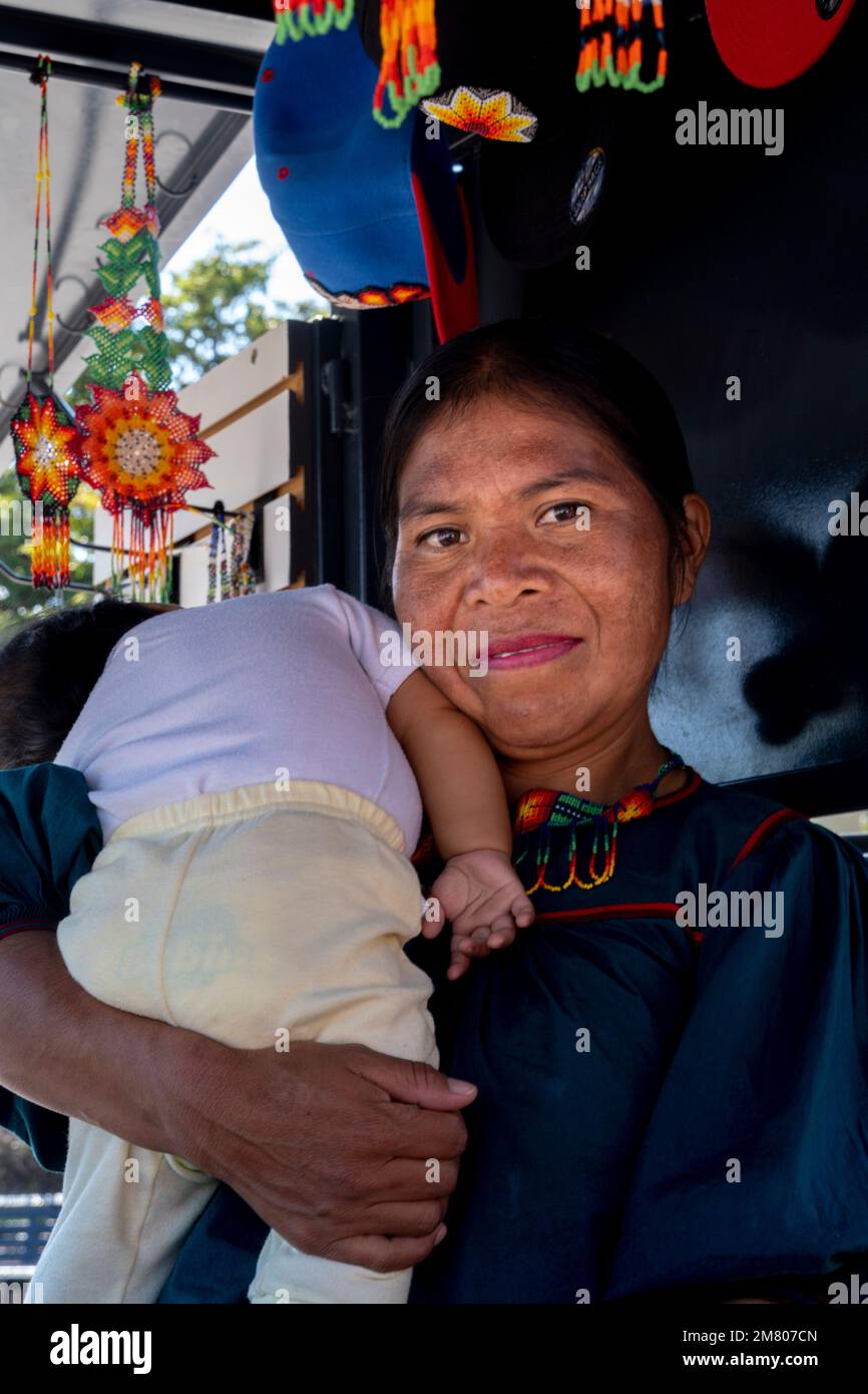traditional artisan woman carrying her daughter, surrounded by her very colorful chaquira handicraft Stock Photo