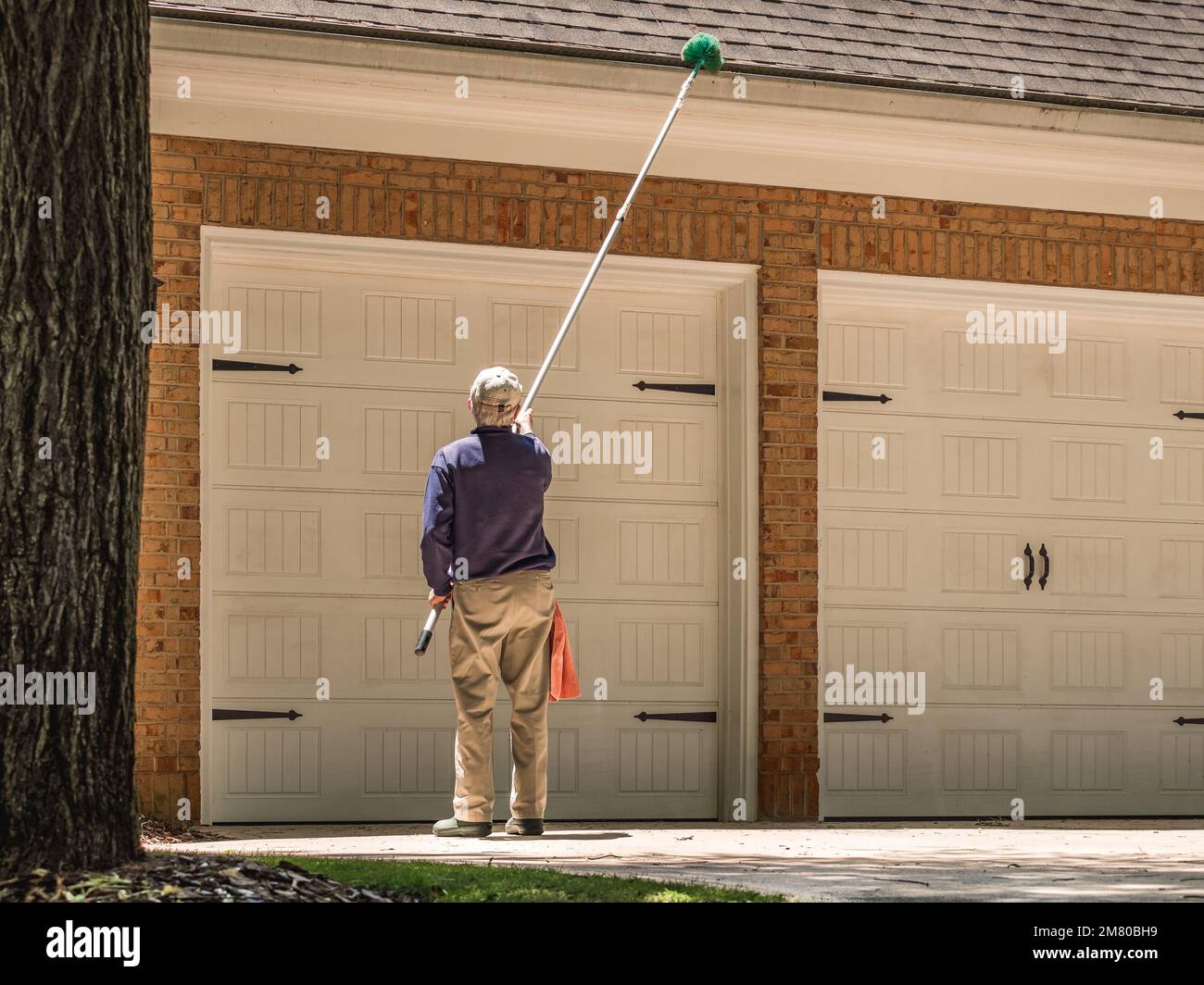 Man cleaning gutters of the house with a long handle broom brush
