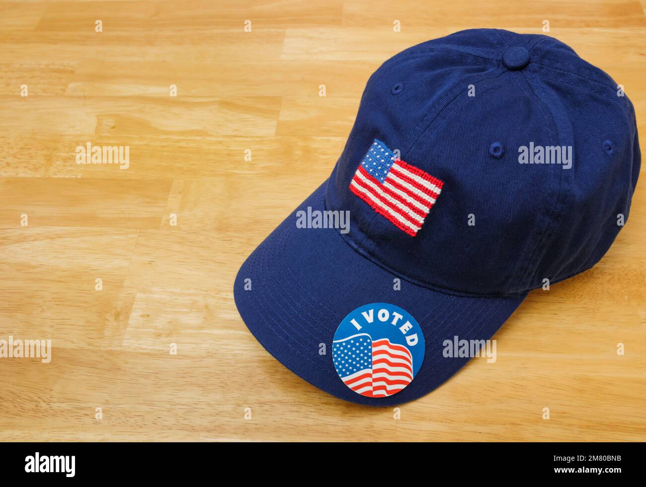 I Voted sticker on a patriotic blue baseball hat with American flag on wood background. Stock Photo
