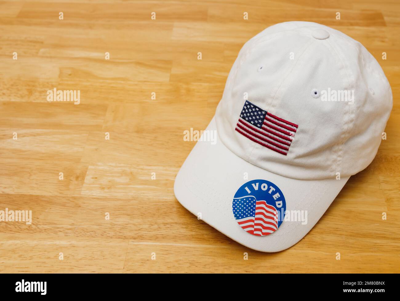 I Voted sticker on a patriotic white baseball hat with American flag on wood background. Stock Photo
