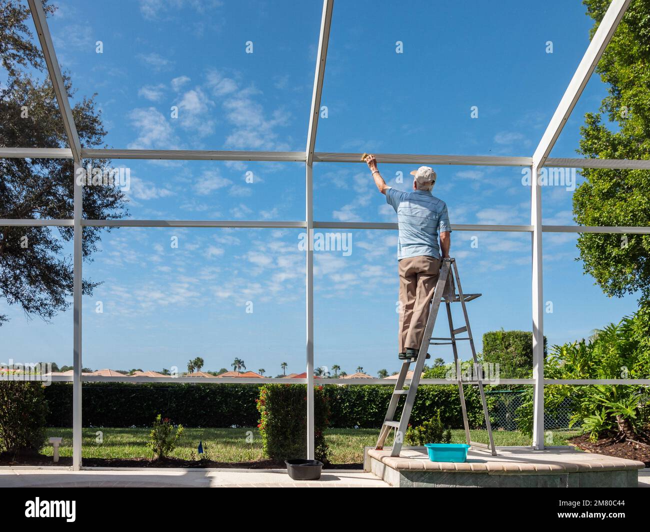 Handyman on ladder cleaning outdoor pool cage enclosure. Screened