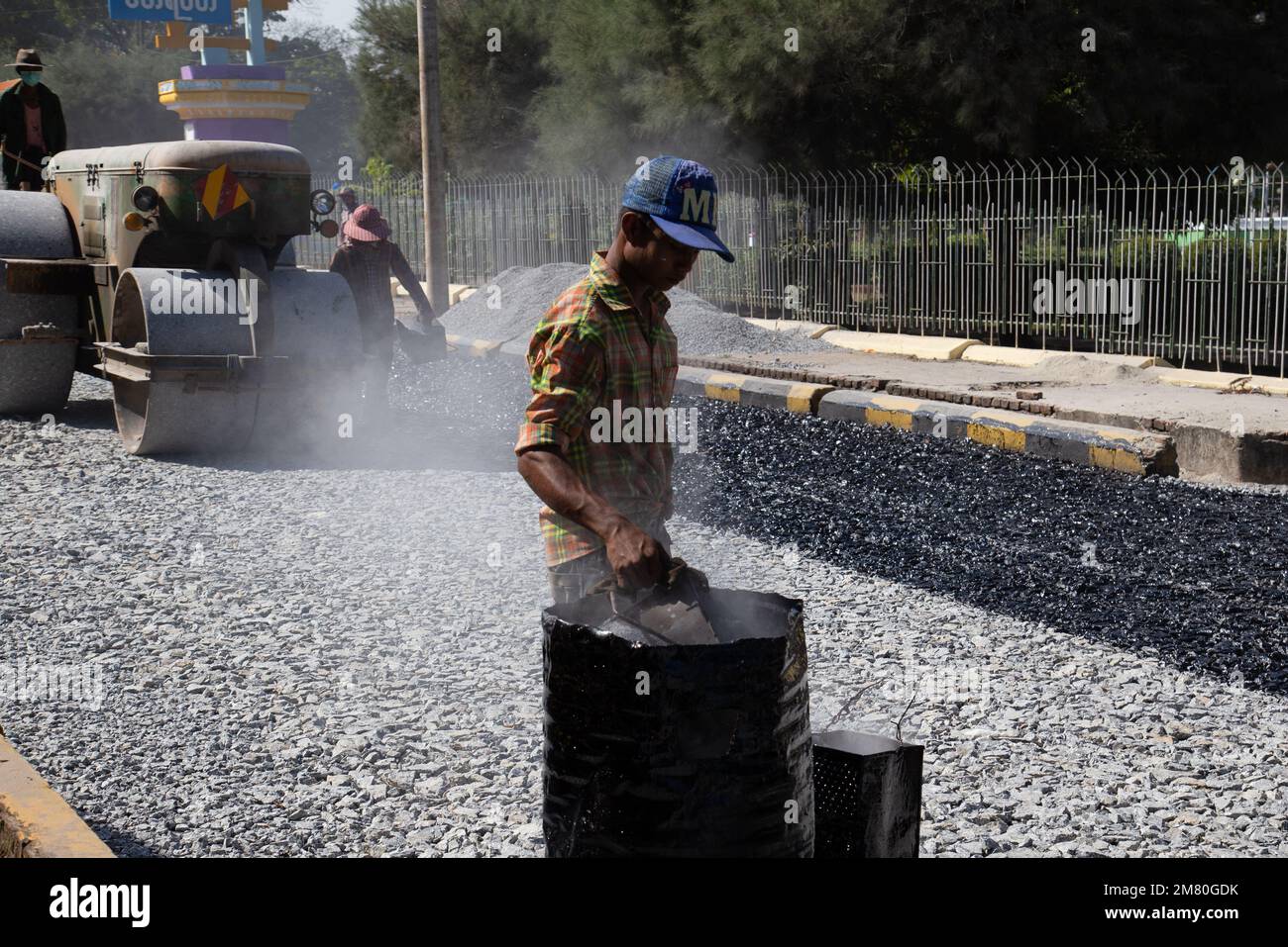 A man walks with melted asphalt. Roads are Paved by Hand in Mawlamyine
