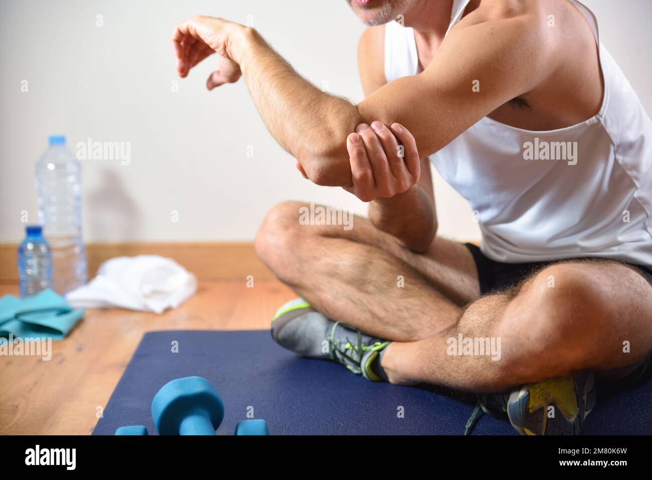 Detail of man doing sports with elbow pain holding himself with his hand sitting on a mat. Side view Stock Photo