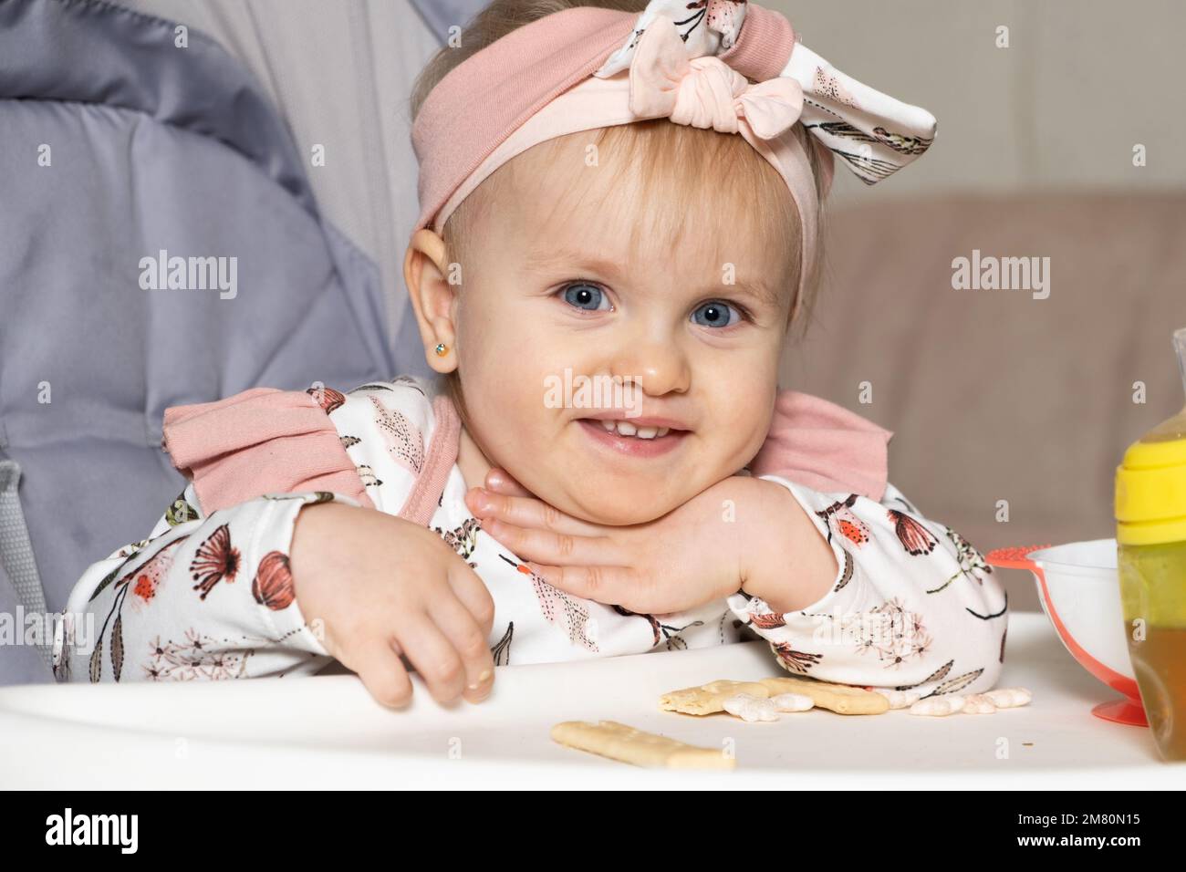 A beautiful oneyearold girl eats cookies sitting in a feeding chair