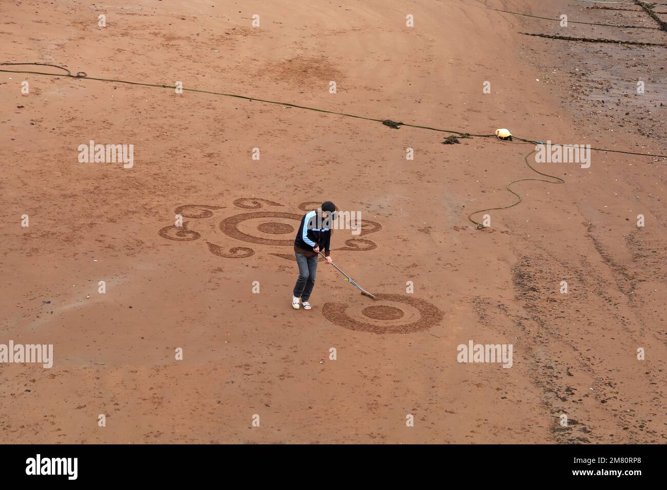 Sand artist creates a design at low tide at Paignton Harbour, Torbay