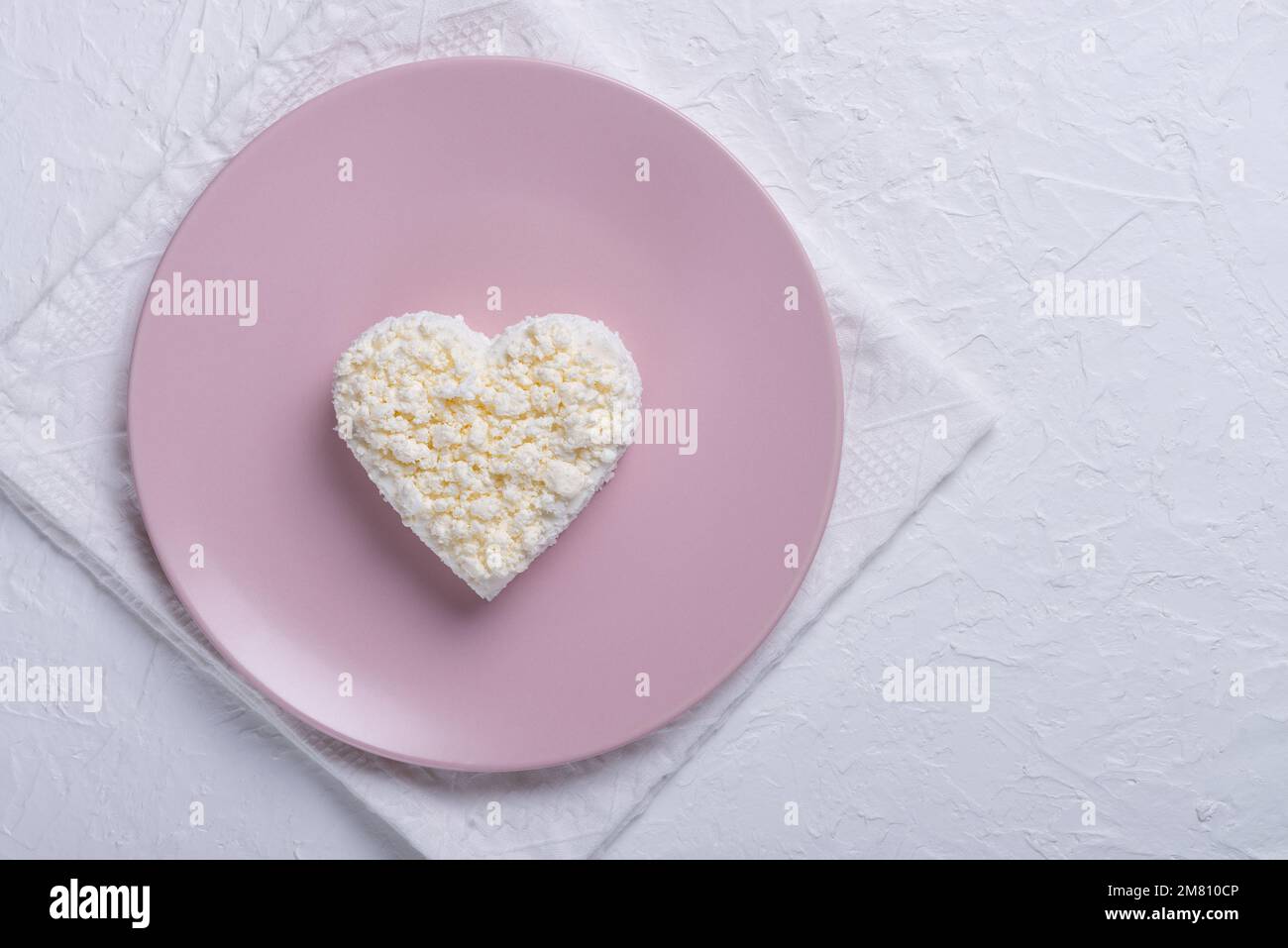 Heart shaped cottage cheese in a pink plate on a white table. Copy space for text Stock Photo