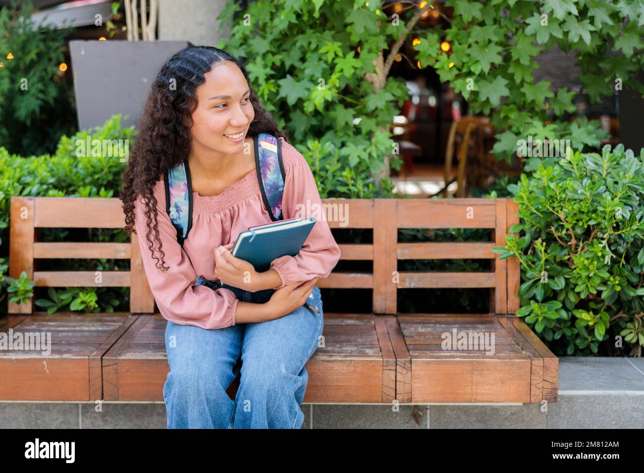 Smiling black student woman sitting and waiting for a classmate outside the mall. Education concept Stock Photo