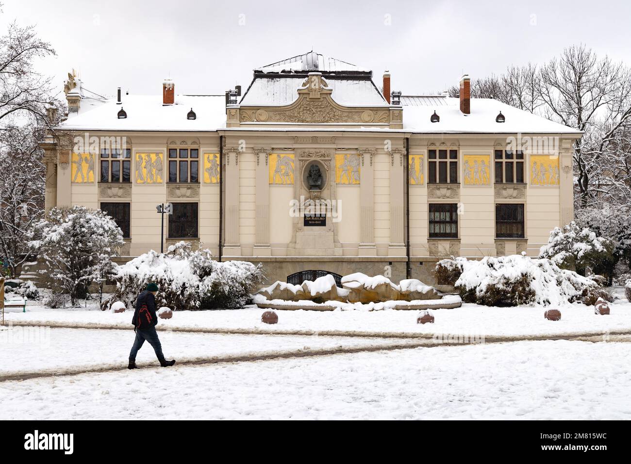 Krakow architecture - a man walking by the exterior of the Art Nouveau style Palace of Fine Art in winter snow, Krakow Old Town, Krakow Poland Stock Photo