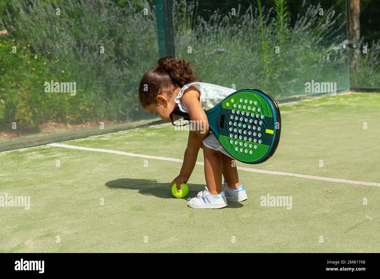 Little girl handing tennis balls to her mother on a padel tennis court
