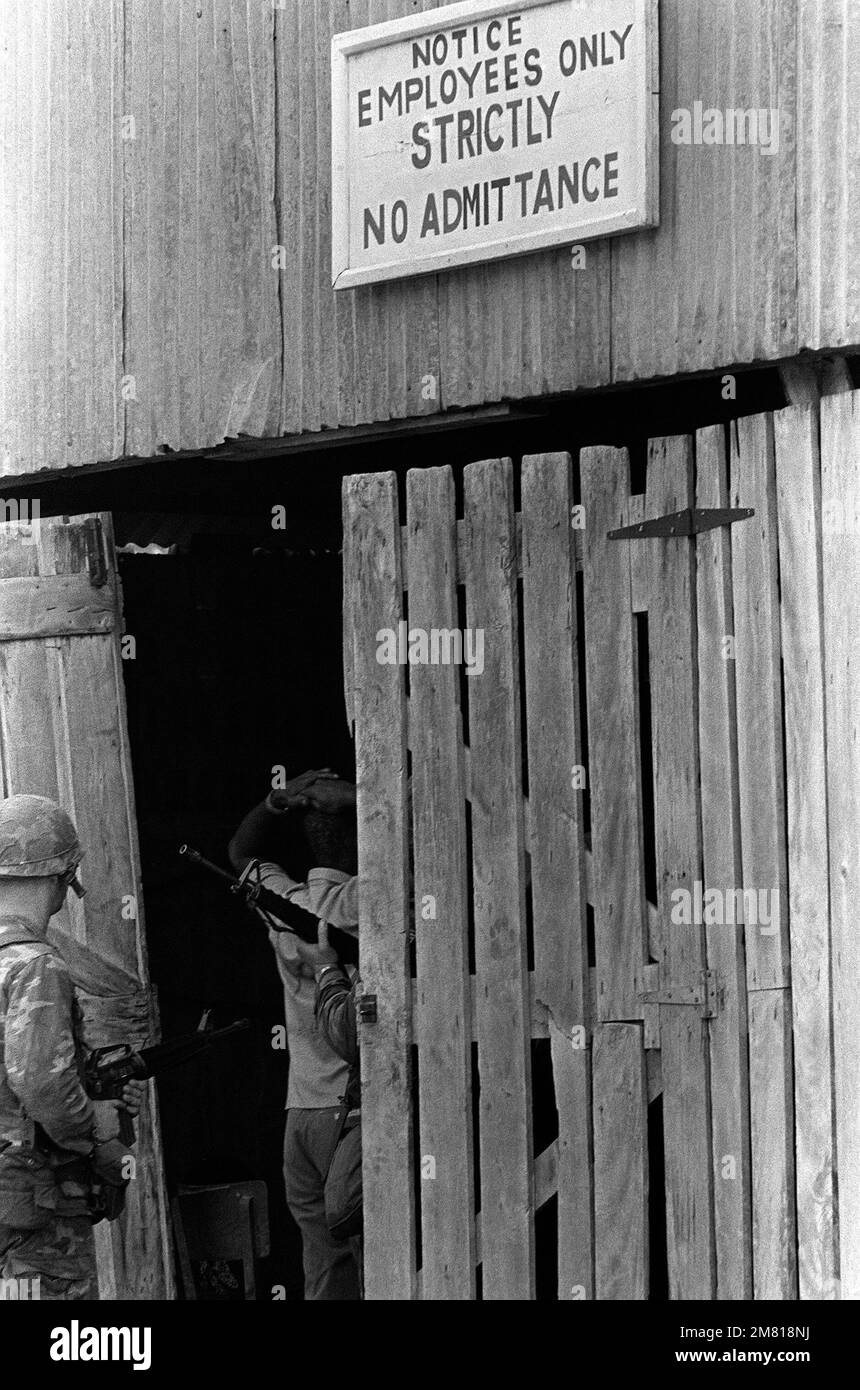 A member of the Peoples Revolutionary Army is escorted by Marines armed with M16A1 rifles, into a building after his capture during Operation URGENT FURY. Subject Operation/Series: URGENT FURY Country: Grenada (GRD) Stock Photo