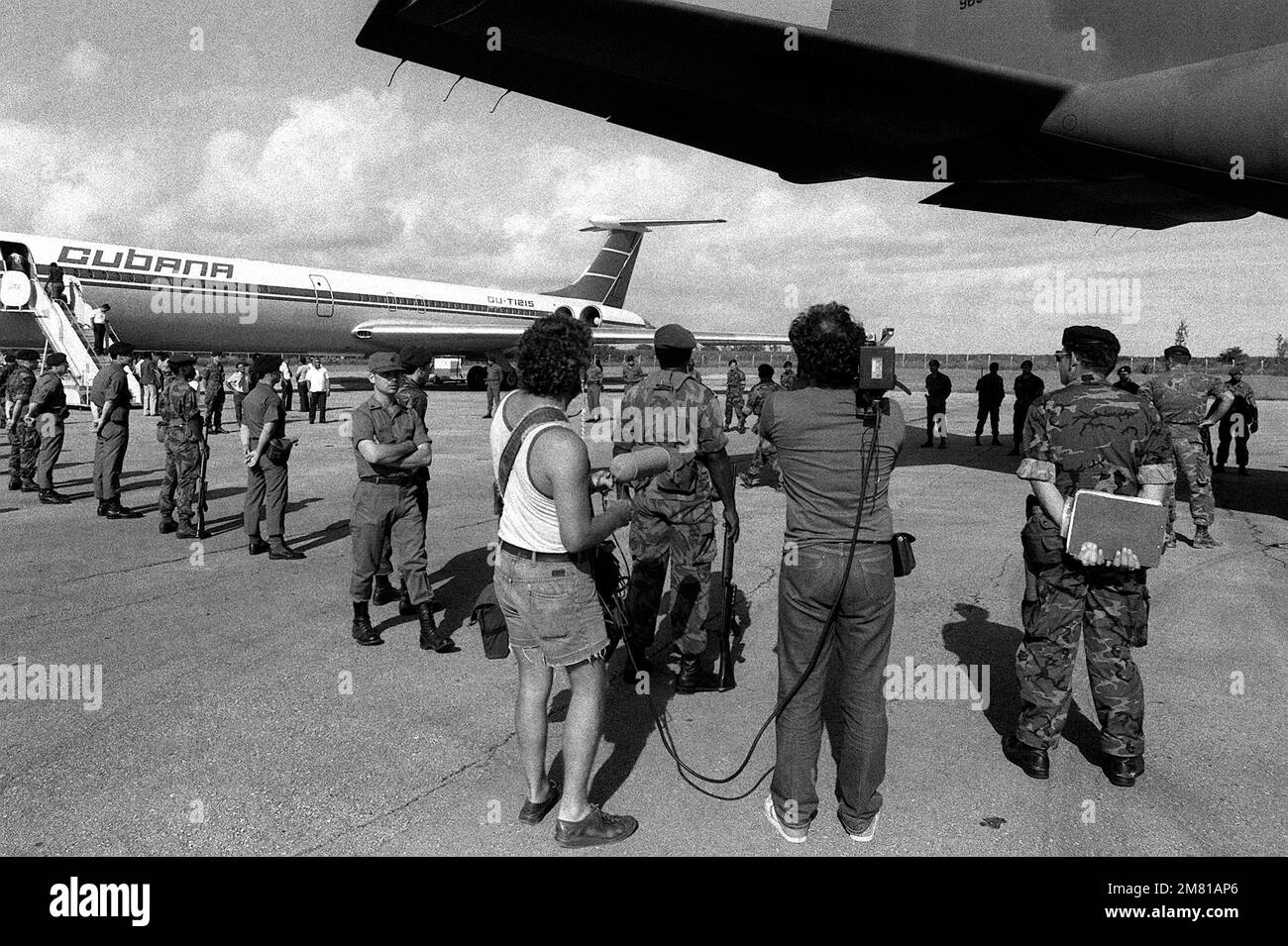 U.S. Air Force security police stand guard as Cuban nationals are transferred from a C-130 Hercules aircraft to a I1-62M airliner. They are being returned to Cuba after being captured on Grenada during the multiservice, multinational Operation Urgent Fury. He is being transferred from the C-130 Hercules aircraft to a Cuban airliner that will return him to Cuba. Subject Operation/Series: URGENT FURY Base: Seawell International Airport Country: Bangladesh (BGD) Stock Photo