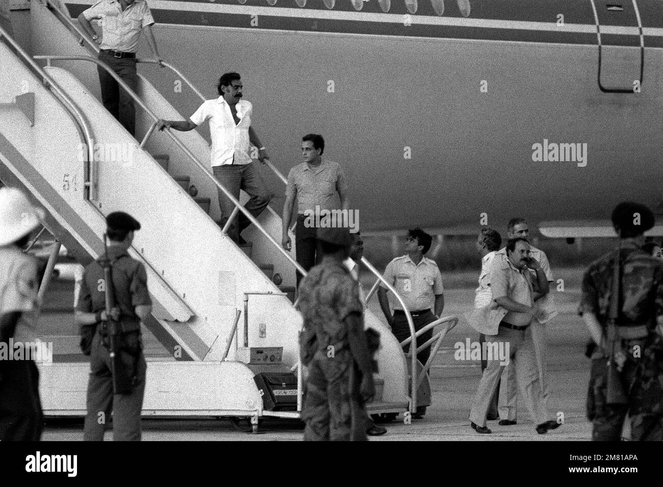 U.S. Air Force security police stand guard over Cuban nationals on the boarding ramp of the Cuban I1-62M airliner that will return them to Cuba. They were captured on Grenada during the multiservice, multinational Operation Urgent Fury. He is being transferred from the C-130 Hercules aircraft to a Cuban airliner that will return him to Cuba. Subject Operation/Series: URGENT FURY Base: Seawell International Airport Country: Bangladesh (BGD) Stock Photo