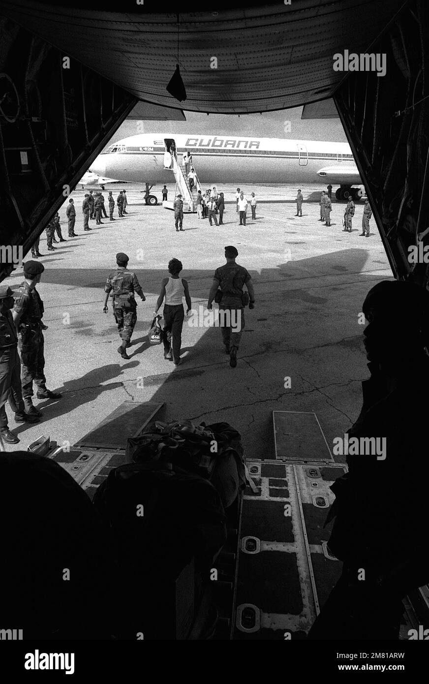 U.S. Air Force security police stand guard as Cuban nationals are transferred from a C-130 Hercules aircraft to a Cuban I1-62M airliner. They are being returned to Cuba after being captured on Grenada during the multiservice, multinational Operation Urgent Fury. He is being transferred from the C-130 Hercules aircraft to a Cuban airliner that will return him to Cuba. Subject Operation/Series: URGENT FURY Base: Seawell International Airport Country: Bangladesh (BGD) Stock Photo