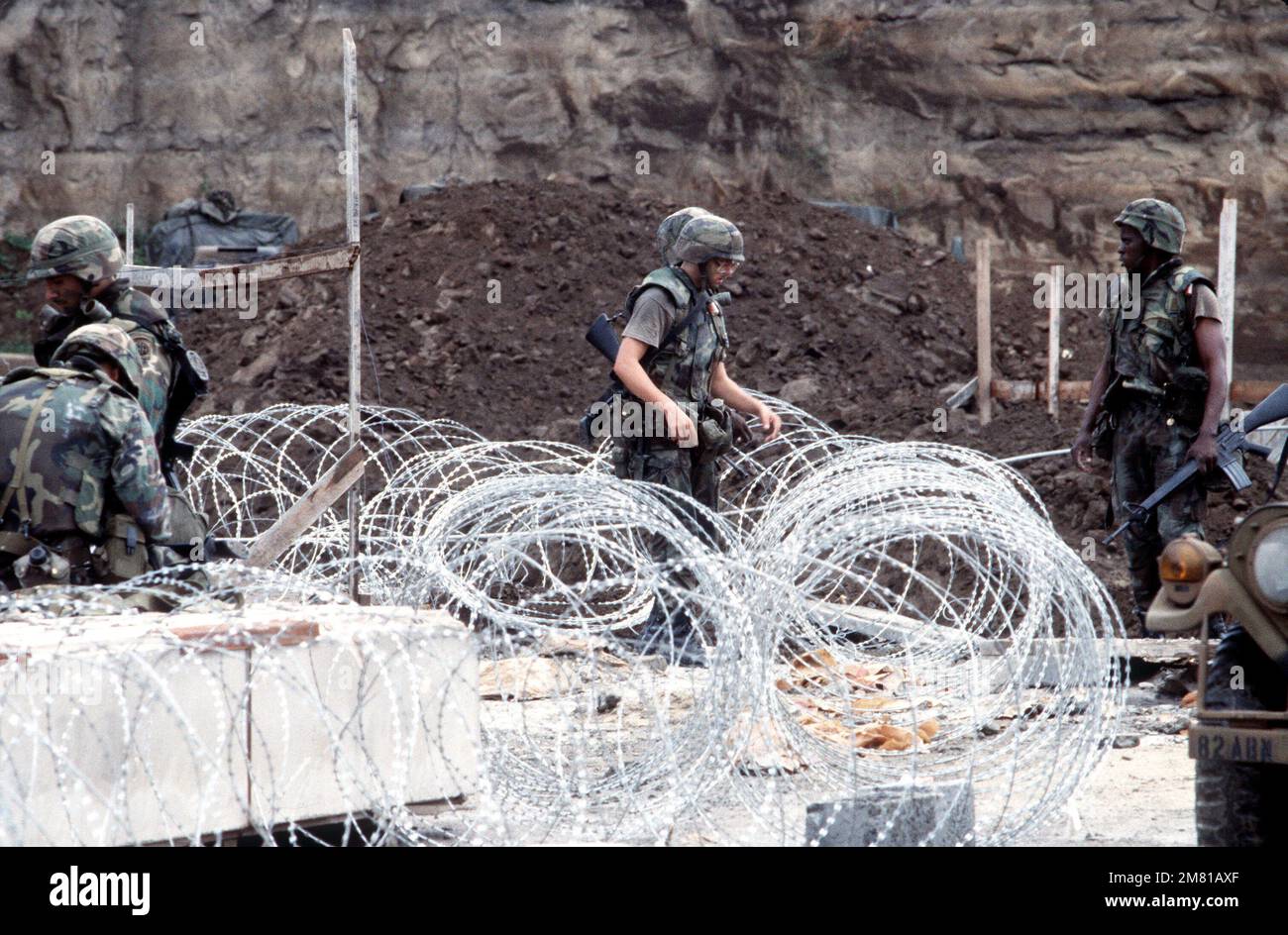 US military personnel, armed with M16A1 rifles, lay concertina wire during Operation URGENT FURY. Subject Operation/Series: URGENT FURY Country: Grenada (GRD) Stock Photo