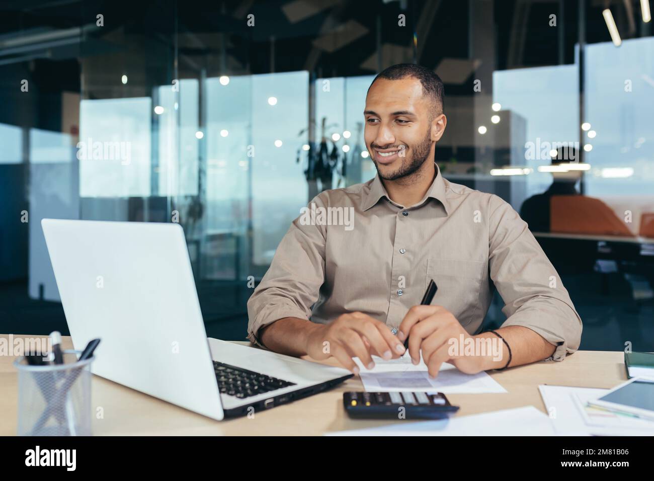 Successful african american businessman inside office doing paperwork, man writing information, worker using laptop for work sitting with bills and contracts smiling and satisfied with result. Stock Photo