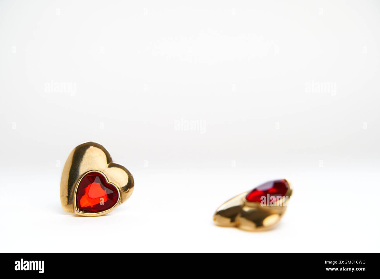 Duel concept. Sad and alone after break up concept. Heart shaped golden jewel with ruby by out of focus earring over white background Stock Photo